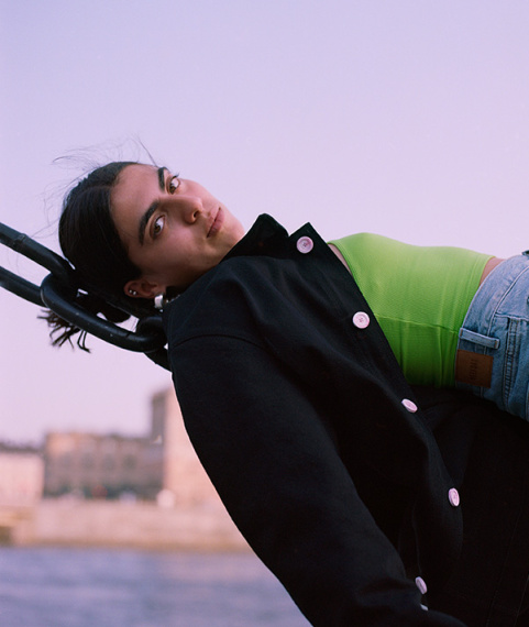 Girl wearing black jacket over a greeen tank and blue denim in front of a natural unset sky