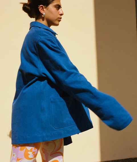 girl wearing blue denim workwear inspired jacket infront of a yellow wall