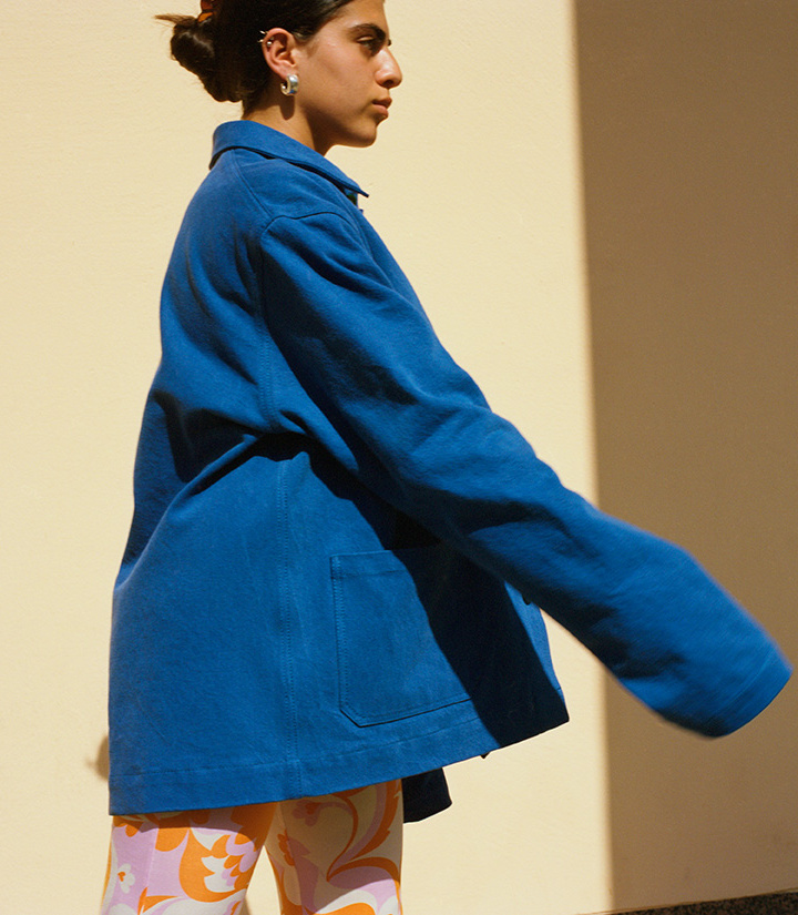 girl wearing blue denim workwear inspired jacket infront of a yellow wall